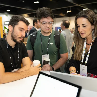 Two men and a woman with coffee cups in head standing around a screen and discussing it's content